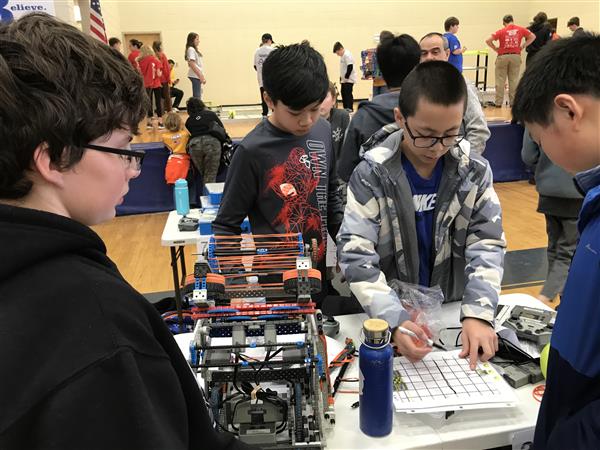 Students at a VEX IQ Robotics competition strategize their game plan around a table.